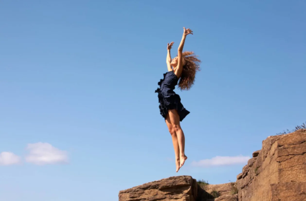 Barefoot woman on rocky cliff jumping for joy while earthing